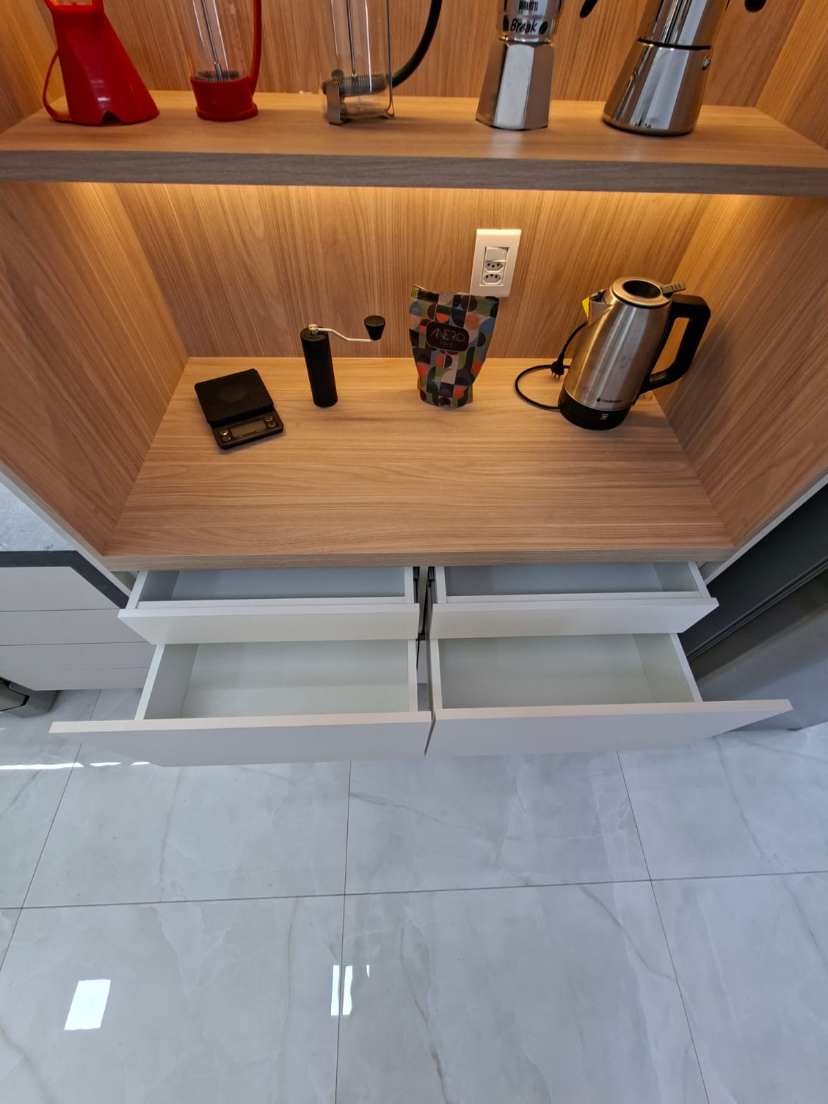 Nicho de madeira iluminado com estação de café, gavetas abertas mostrando o acabamento interno