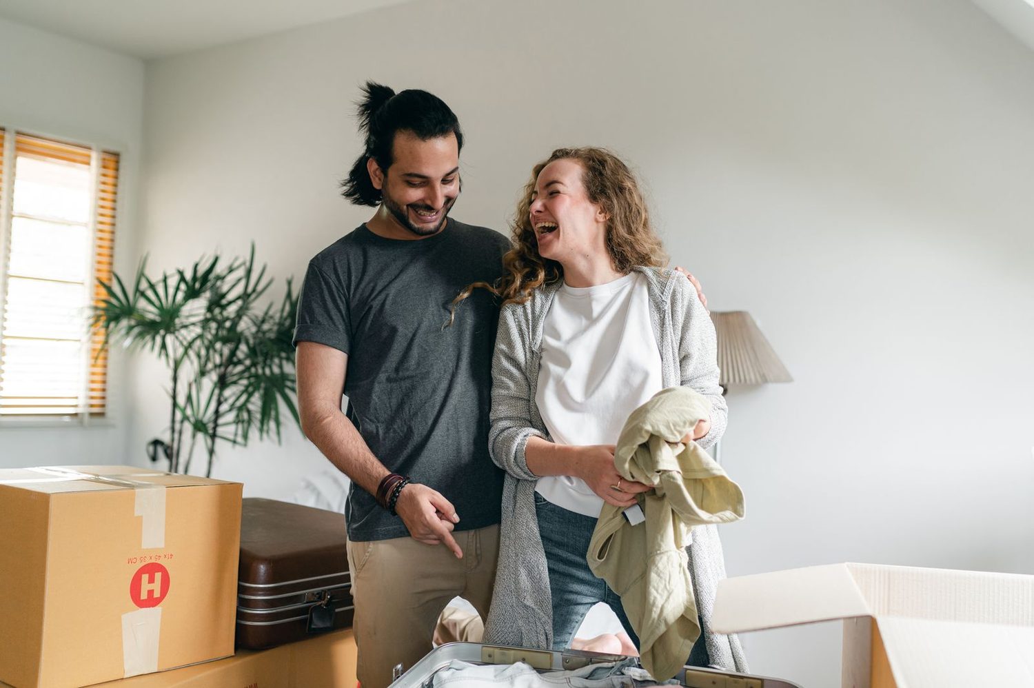 Casal sorrindo entre caixas de mudança no apartamento novo